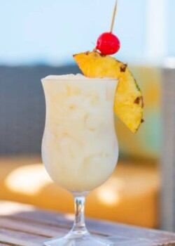 Glass of spritz aperol with orange slice against poolside at resort hotel during vacation. Elegant goblet of sparkling wine and orange juice on background of blue water outdoor. Relaxation and travel.